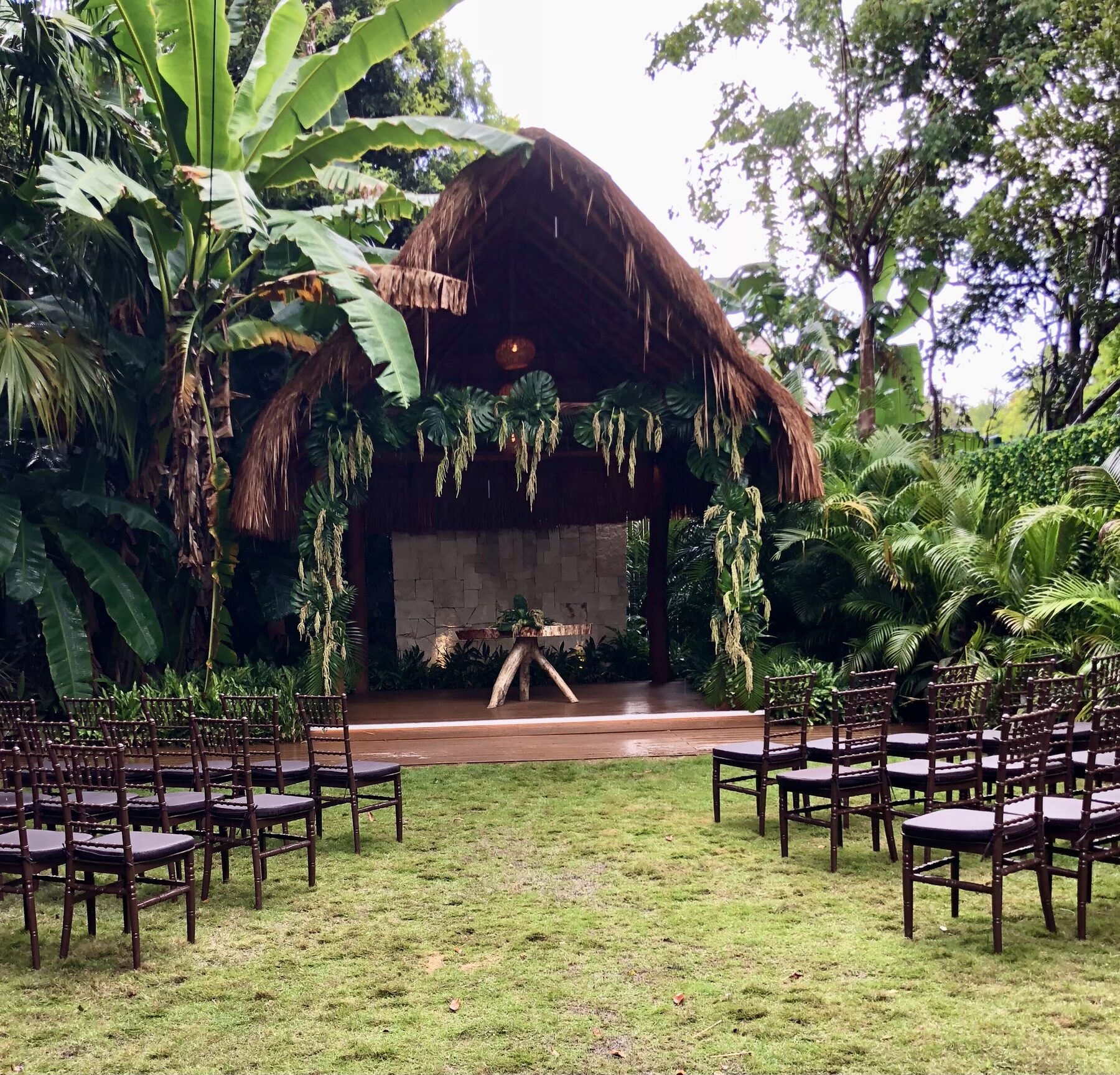 A tropical thatched pavilion ceremony with rows of chairs on a lawn