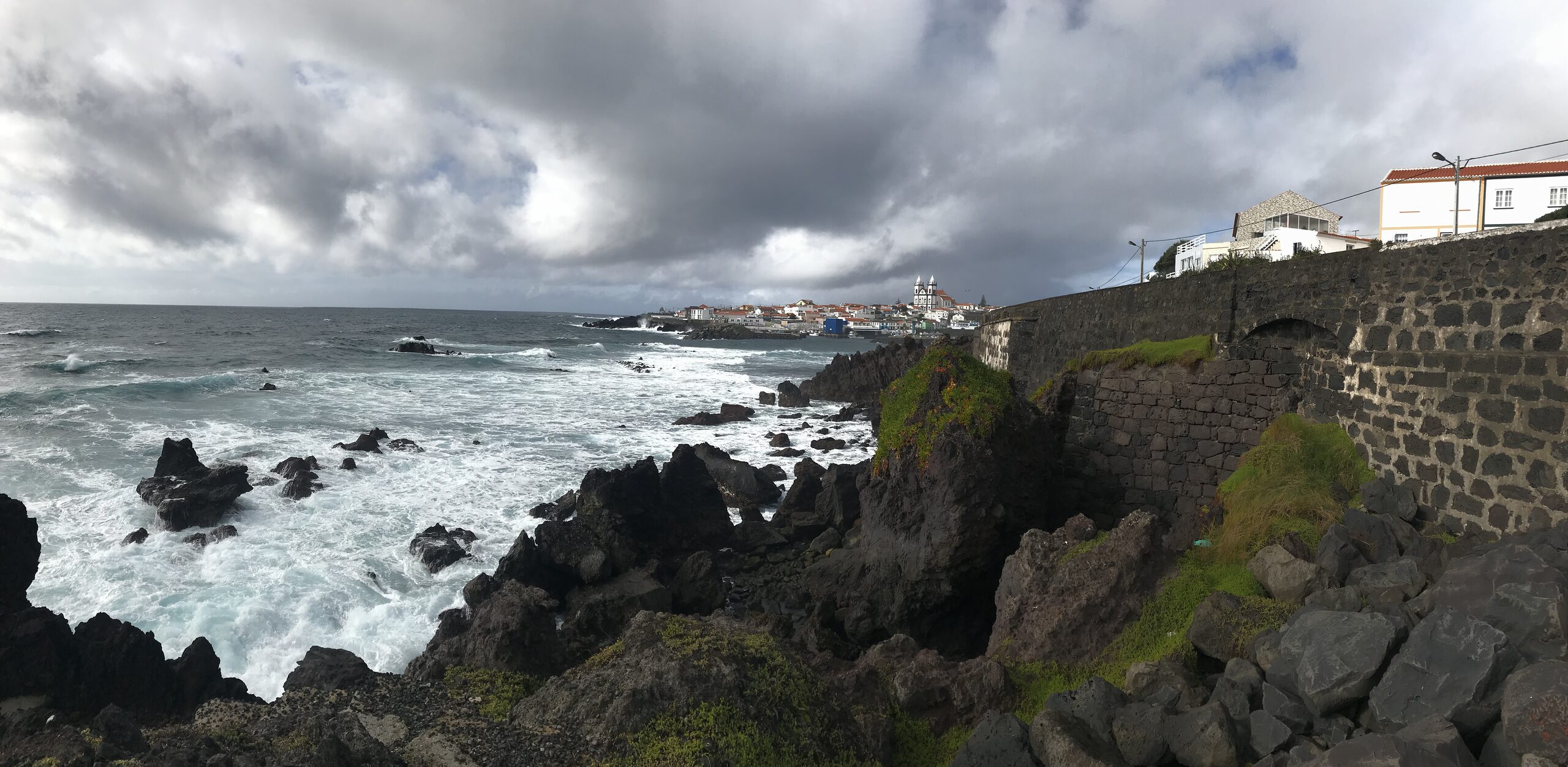 A coastal village on volcanic rock, waves breaking under a dramatic sky