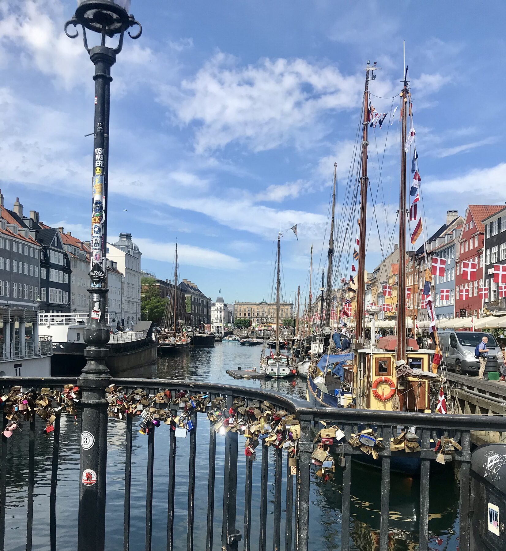 A historic canal lined with boats, flags, and love locks on a bridge
